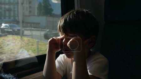Téléchargez les photos : Enfant endormi se réveillant de la sieste dans le train, se protégeant du soleil. petit garçon frotter les yeux avec la main tout en voyageant - en image libre de droit