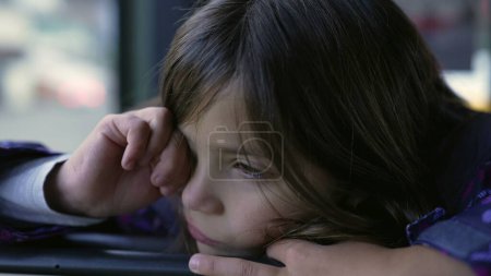 Photo for Tired little girl rubbing eye while on a moving bus, 8 year odl child leaning on bus seat rubs face with hand wanting to nap - Royalty Free Image