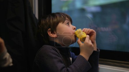 Foto de Thoughtful little boy snacking corn while looking at scenery pass by from inside train - Imagen libre de derechos