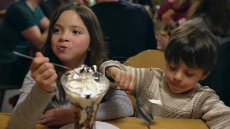 Foto de Kdis comer helado de crema batida en el restaurante, hermano y hermana compartir la indulgencia dulce de azúcar en el restaurante en la salida de fin de semana por la noche - Imagen libre de derechos