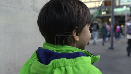 Photo for Back of child walking in train platform station heading to city. Young boy walks forward wearing raincoat - Royalty Free Image