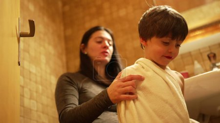 Téléchargez les photos : Moment d'amour post-bain - Mère embrasser fils sur la joue tout en séchant son corps enveloppé de serviettes - en image libre de droit