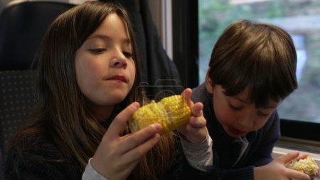 Photo for Children snacking corn inside moving train, siblings - small brother and sister eating healthy food inside high speed transportation - Royalty Free Image