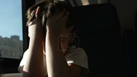 Téléchargez les photos : Épuisé enfant frotter les yeux sur le train en mouvement, se réveiller de la sieste par la fenêtre tout en voyageant, se protégeant des rayons du soleil - en image libre de droit