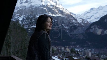 Foto de Contemplative happy woman enjoying a beautiful view of mountains in Switzerland standing by balcony taking the fresh air of the alps - Imagen libre de derechos
