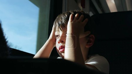Photo for Exhausted child rubs eyes and face while on a moving train, passenger kid wakes up from nap while traveling feeling tired by window - Royalty Free Image