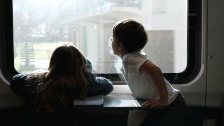 Téléchargez les photos : Enfants assis par la fenêtre du train, petit frère couvrant le visage et les yeux des rayons du soleil tout en voyageant avec sœur. Famille en vacances - en image libre de droit