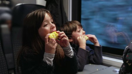 Téléchargez les photos : Little Siblings Eating Healthy Corn Snacks During Train Travel - en image libre de droit