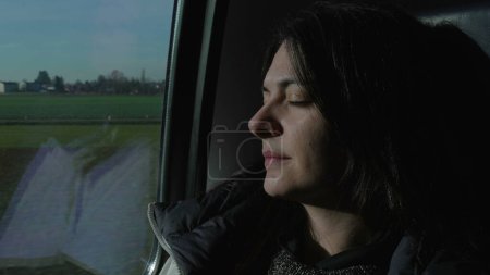 Foto de Female passenger asleep by train window while traveling. Woman commuter napping while landscape passes by in background - Imagen libre de derechos