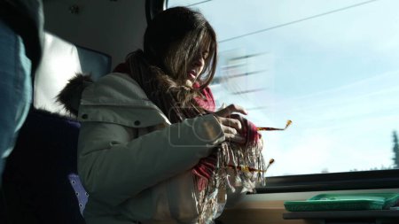 Foto de Woman cleaning sunglasses with scarf while traveling by train. Female passenger commuter wiping dust from eye wear inside Swiss highspeed transportation - Imagen libre de derechos