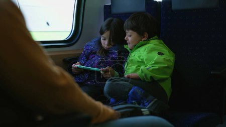Photo for Young Brother and sister engaged with portable handheld video game console inside train. Children engaged with technology inside high speed transportation - Royalty Free Image