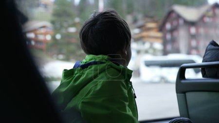 Foto de Niño observando la ciudad desde el asiento de la ventana del autobús usando impermeable. Pasajero Niño pequeño mirando desde el transporte público - Imagen libre de derechos
