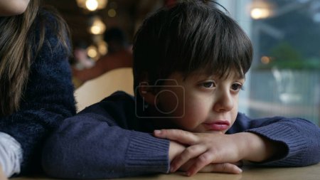 Foto de Muchacho aburrido quejándose, niño enfurruñado sintiéndose molesto apoyado en la mesa del restaurante, cara de niño primer plano - Imagen libre de derechos