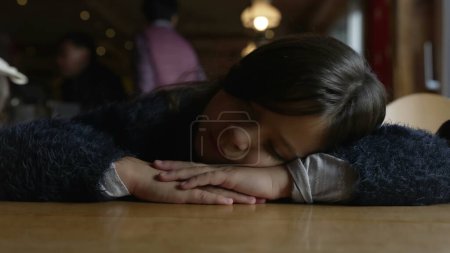 Foto de Un niño deprimido con la cabeza puesta en la mesa sintiendo profunda tristeza, primer plano de niño melancólico de 8 años en el restaurante del restaurante - Imagen libre de derechos