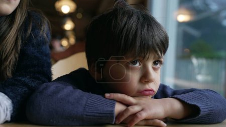 Foto de Muchacho aburrido quejándose, niño enfurruñado sintiéndose molesto apoyado en la mesa del restaurante, cara de niño primer plano - Imagen libre de derechos