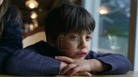 Téléchargez les photos : Petit garçon ennuyé se plaignant, enfant boudant se sentant ennuyé s'appuyant sur la table du restaurant, gros plan visage d'enfant - en image libre de droit