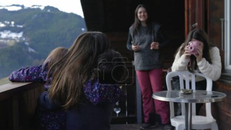 Téléchargez les photos : Enfants posant pour la photo dans le balcon du chalet, la mère prend des photos d'enfants avec un appareil photo instantané polaroïd pendant les vacances en famille en hiver saison de ski - en image libre de droit
