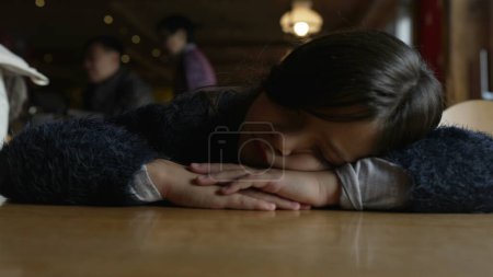 Téléchargez les photos : Un enfant déprimé avec la tête posée sur la table ressentant une profonde tristesse, gros plan de l'enfant mélancolique de 8 ans au restaurant - en image libre de droit