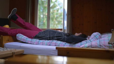Foto de Relajada mujer Descansando en acogedor chalet suizo de montaña, vacaciones en familia en casa de madera, persona se acuesta en la cama - Imagen libre de derechos