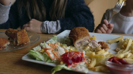 Photo for Kids enjoying food at restaurant, little girl eating milanese meat with french fries. Children at diner during lunch time - Royalty Free Image