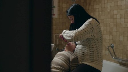 Téléchargez les photos : Mère franche brossant les pieds de l'enfant dans la salle de bain avant de se coucher. Soins d'hygiène dentaire parentale dans la routine du soir - en image libre de droit