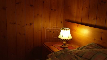 Photo for Child turns on bedside lamp inside traditional wooden chalet interior. One little boy turning ON traditional antique light - Royalty Free Image
