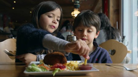 Téléchargez les photos : Enfants mangeant de la nourriture au restaurant, frères et sœurs - petit frère et sœur dégustant des frites et des repas de poulet au dîner à l'intérieur en bois - en image libre de droit