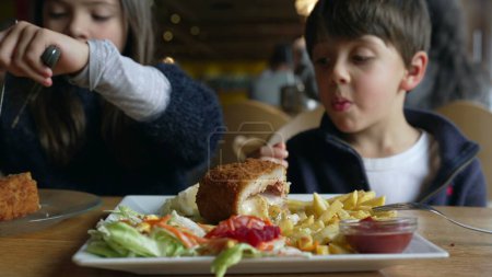Téléchargez les photos : Enfants au restaurant devant le cordon bleu avec des frites. Frères et sœurs - petit frère et petite sœur mangeant de la nourriture au dîner, appréciant l'heure du repas - en image libre de droit