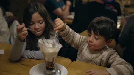 Photo for Youthful Joy in Sweet Treat - Young Brother and Sister Savoring Whipped Cream Sundae at Local Diner on Weekend Night - Royalty Free Image