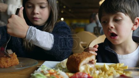 Téléchargez les photos : Enfants au restaurant devant le cordon bleu avec des frites. Frères et sœurs - petit frère et petite sœur mangeant de la nourriture au dîner, appréciant l'heure du repas - en image libre de droit