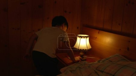 Foto de Niño enciende la lámpara de noche dentro del interior tradicional chalet de madera. Un niño pequeño encendiendo la luz antigua tradicional - Imagen libre de derechos