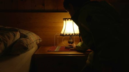 Téléchargez les photos : Enfant éteignant la lampe de chevet - la lumière orange devient sombre lorsque la personne éteint la lumière - en image libre de droit