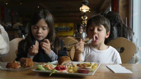 Foto de Niños comiendo comida en la cafetería, niños disfrutando de un restaurante acogedor, hermanos, hermano pequeño y hermana - Imagen libre de derechos