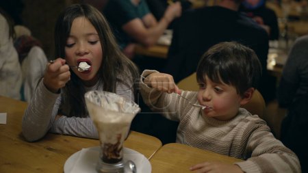 Photo for Youthful Joy in Sweet Treat - Young Brother and Sister Savoring Whipped Cream Sundae at Local Diner on Weekend Night - Royalty Free Image