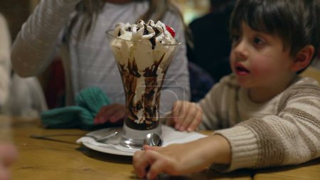 Photo for Serving ice cream sundae at restaurant table, children grabbing spoons and eating dessert at diner in the evening, siblings enjoy sugar sugary food with whipped cream - Royalty Free Image
