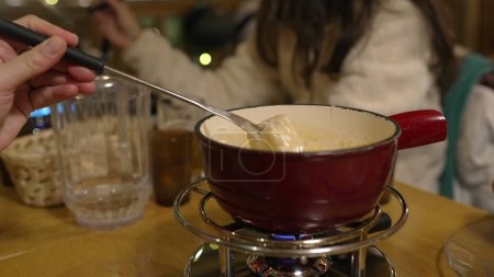 Photo for Closeup of fondue at restaurant - tradition Swiss cheese cuisine at diner. Pot underneath heater with fork dipping piece of bread into melted cheese - Royalty Free Image