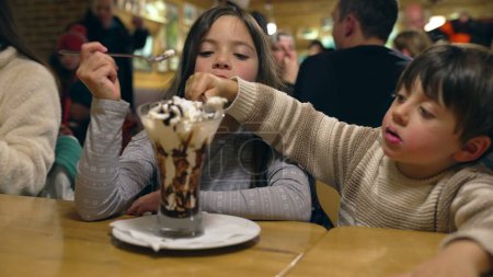 Photo for Siblings Sharing Ice Cream with Whipped Cream at Restaurant Diner - Children Enjoying Sugar Dessert Treat Indulgence - Royalty Free Image