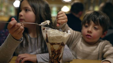 Téléchargez les photos : Enfants se livrant à sundae crème glacée avec crème fouettée. frère et soeur profiter du dessert - en image libre de droit