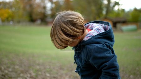 Téléchargez les photos : 4 ans petit garçon promenades dans le parc naturel à l'extérieur regardant vers le bas à l'herbe veste automne automne saison - en image libre de droit