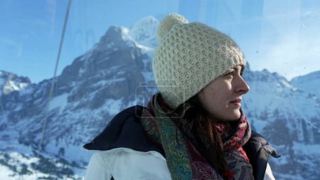 Foto de Mujer vistiendo ropa de invierno disfrutando de la vista de los Alpes suizos desde lo alto en el pico de la montaña mirando la vista panorámica - Imagen libre de derechos