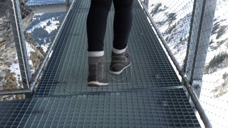 Téléchargez les photos : Personne marchant soigneusement à travers le support de main courante en métal par la falaise dans l'aventure des Alpes suisses, vue rapprochée de la femme prudente effrayée par la vue sur la montagne élevée - en image libre de droit