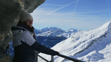 Téléchargez les photos : Femme bénéficiant d'une vue panoramique sur les Alpes suisses vue sur la montagne debout à côté de la falaise dans le support de main courante en métal surélevé pendant la saison d'hiver - en image libre de droit