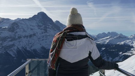 Téléchargez les photos : Retour de la personne regardant la vue panoramique sur les montagnes couvertes de neige à la première plate-forme d'observation emblématique de Grindelwald Superbe panorama alpin, vêtu de vêtements d'hiver - en image libre de droit