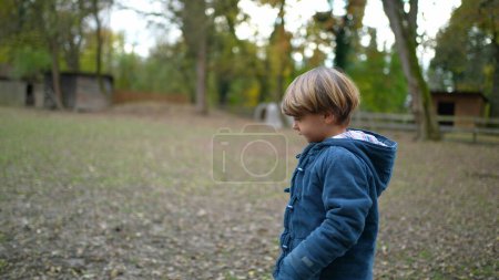 Photo for Child walks in outdoor park during autumn fall season wearing jacket. Profile body of little boy walking in nature - Royalty Free Image