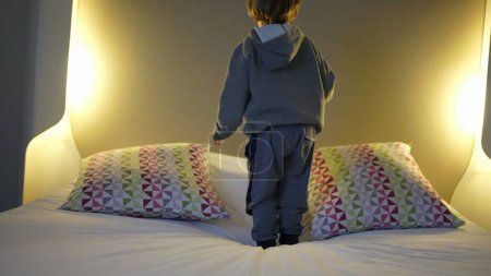 Foto de Niño alegre saltando en la cama del hotel - Diversión de vacaciones. Pequeño niño rebotando arriba y abajo - Imagen libre de derechos