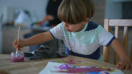 Téléchargez les photos : Enfant engagé dans la peinture artistique à la maison - Laver le pinceau à l'eau, enfant rinçant le pinceau alors qu'il est plongé dans la peinture créative - en image libre de droit
