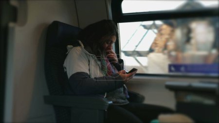 Photo for Commuter Using Smartphone on Train with Window View. Female passenger holding phone inside European transportation - Royalty Free Image