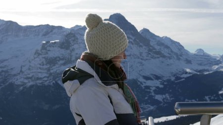 Téléchargez les photos : Portrait de femme dans la trentaine debout par temps froid pendant la saison d'hiver surplombant les montagnes alpines couvertes de neige en toile de fond. personne portant un bonnet et une veste - en image libre de droit