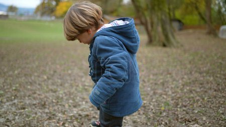 Photo for Little boy lifting feet checking dirty shoes outside at park during autumn fall season. Kid stepping in poop - Royalty Free Image