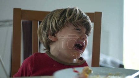 Téléchargez les photos : Petit garçon en colère à table. gros plan visage de l'enfant frapper la table et pleurer mécontent et avec la bouche salissante - en image libre de droit